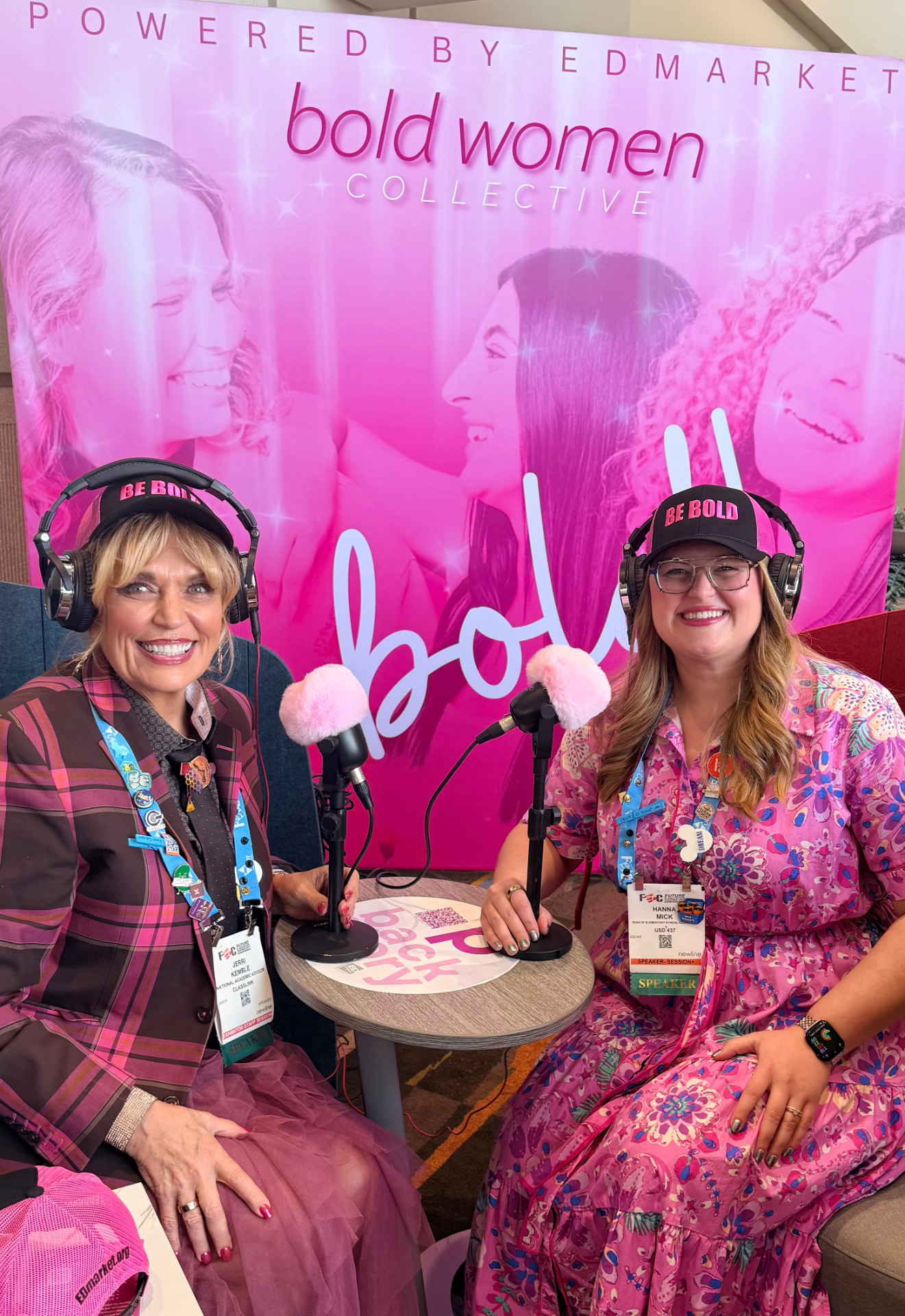 Jerri recording a podcast conversation with a fellow educator at the Bold Women Collective booth, both wearing 'Be Bold' hats and headphones.