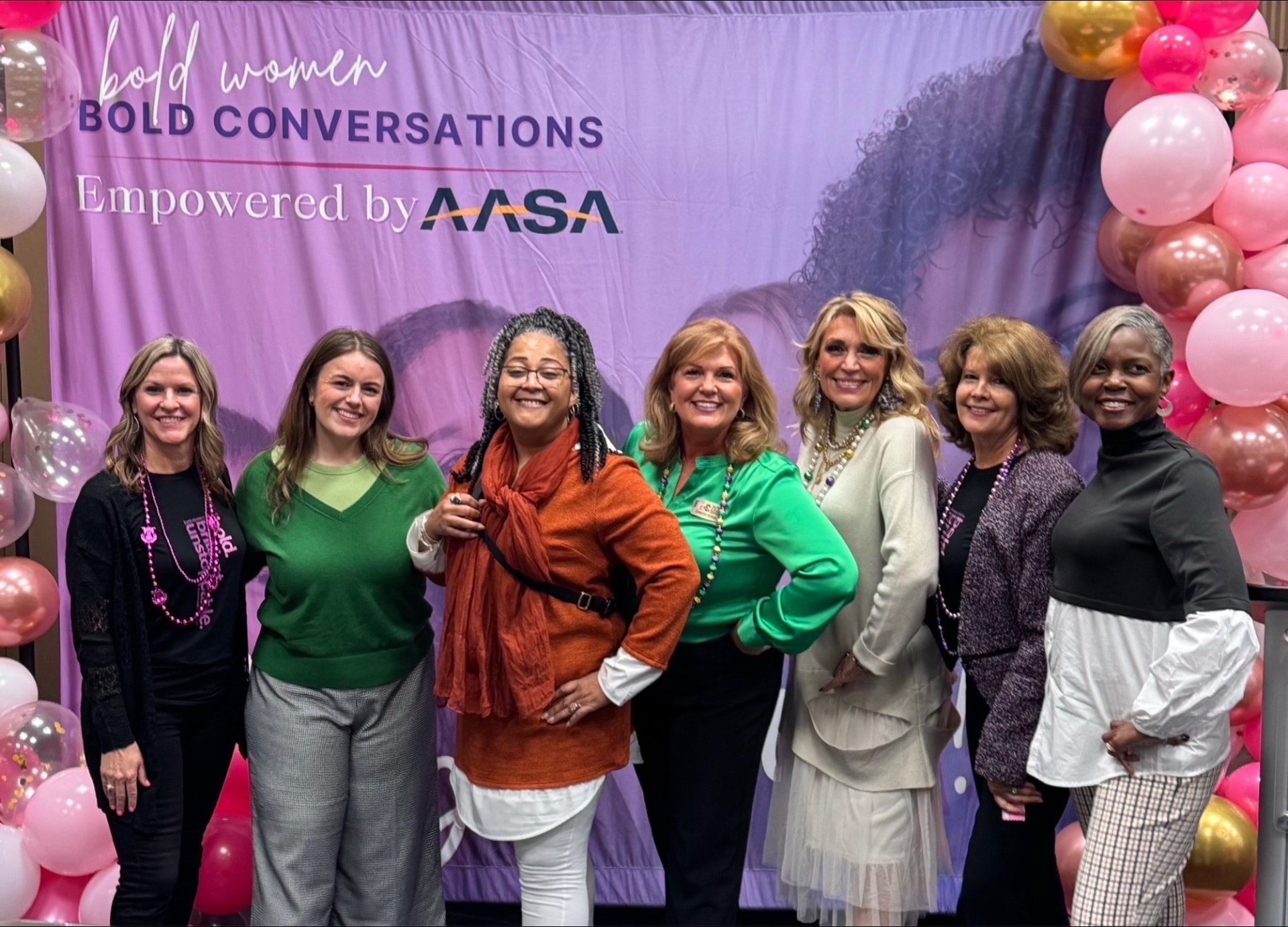 Jerri with a lineup of women leaders in front of the Bold Women, Bold Conversations backdrop, arms linked, laughing.