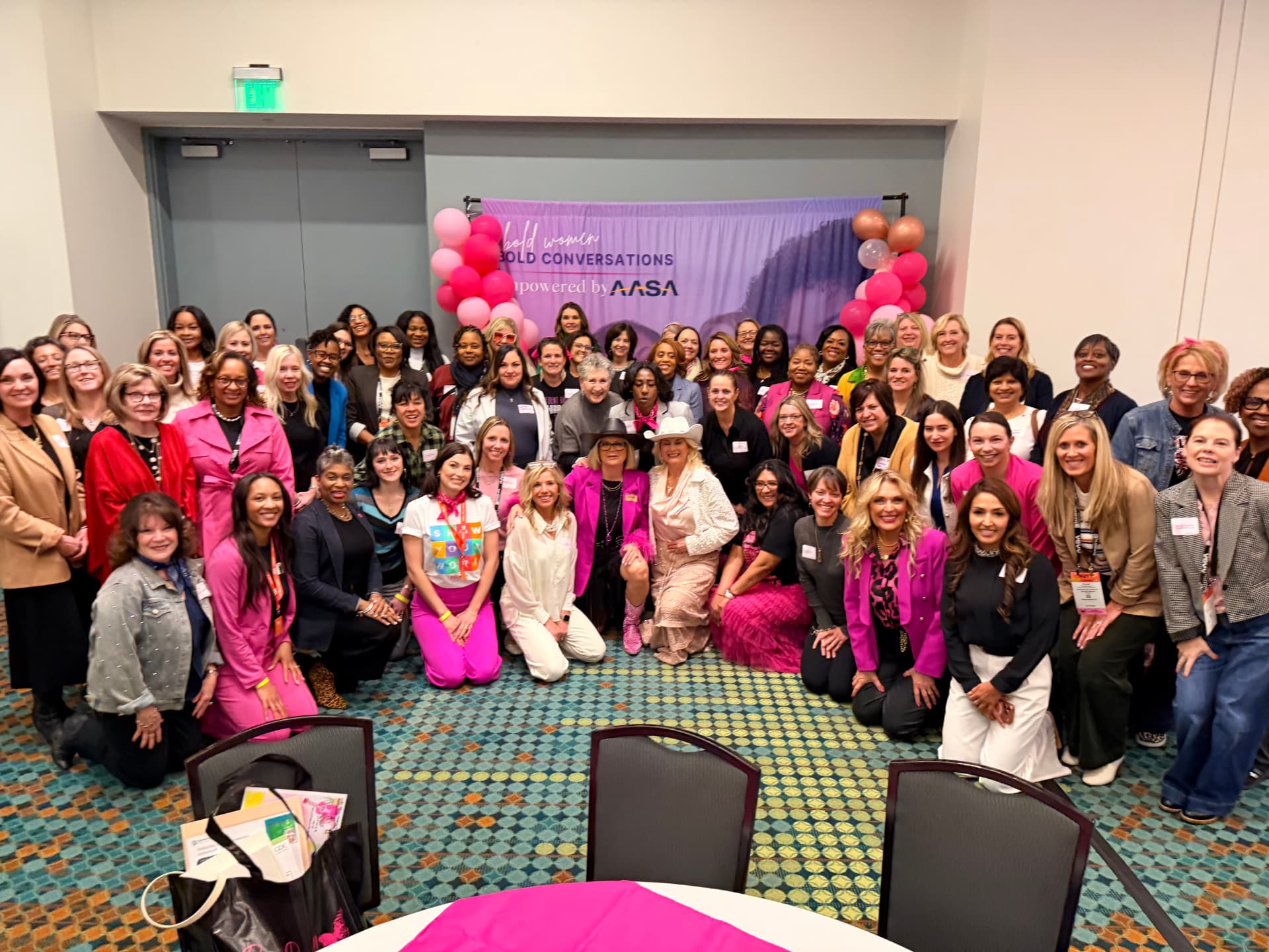 Jerri surrounded by a full room of leaders at the Bold Women, Bold Conversations gathering — dozens of participants smiling together in front of a purple AASA backdrop.